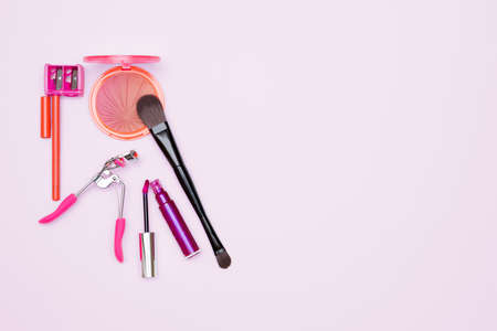 makeup set consisting of a rouge, a brush, a eyelash curler, a lip liner, a sharpener and a pink gloss, isolated on a pink backgroundの写真素材