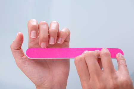 closeup of hands of a young woman filing her nails with french manicure with a pink nail file - focus on the middle finger of the left handの写真素材