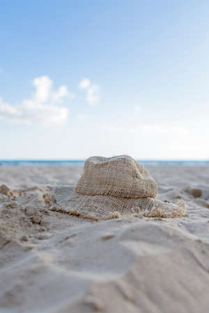lonely raffia hat on the sand of the beach on a sunny day with the sea and the sky backgroundの写真素材