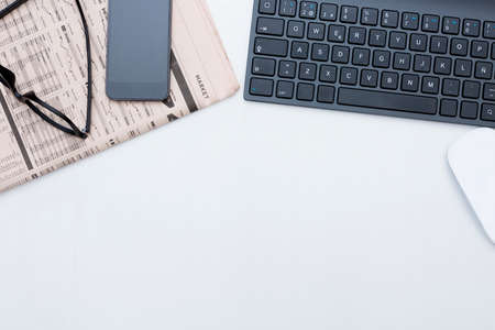 zenithal view of a business desk consisting on a black keyboard, a financial newspaper, a mobile phone, a wireless mouse and a black eyeglasses on a grey desk background - suitable for copy spaceの写真素材