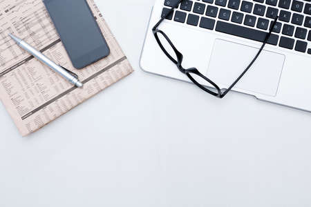 zenithal view of a business desk consisting on a laptop, a financial newspaper and a pen, a mobile phone and a black eyeglasses on a grey desk background - suitable for copy spaceの写真素材