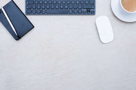 zenithal view of a business desk consisting on a wireless mouse, a cup of coffee with a coffee saucer, a keyboard, and a book calendar with a pen, on a beige desk background - suitable for copy spaceの写真素材