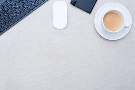 zenithal view of a closeup of a business desk consisting on a cup of coffee with a coffee saucer, a wireless mouse, a keyboard, and a book calendar on a beige desk background - suitable for copy spaceの写真素材