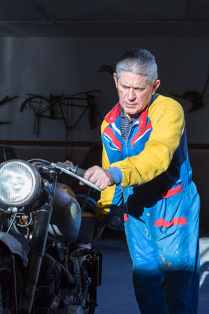 middle aged man pushing a classic motorcycle to place it into the work platform at his workshop ready to start to restore - focus on the manの写真素材