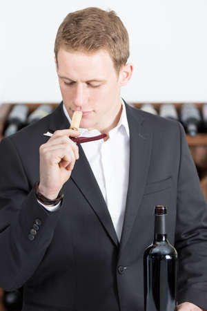 young man on a wine tasting session is smelling a cork stopper of a bottle of a red wine attached to an opener at a restaurant - focus on the man faceの写真素材