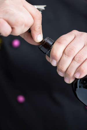 closeup of the hands of a young man uncorking a bottle of red wine is drilling the cork with a corkscrew - focus on the right forefingerの写真素材