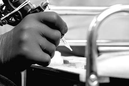 closeup of the hand of a tattoo artist is ink filling a tattoo machine from a ink cup in a tattoo session at the tattoo shop - focus on the tip of the needleの写真素材