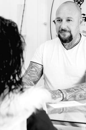 young male tattoo artist is attending to a young female customer before the tattoo session at the tattoo shop - focus on the man faceの写真素材