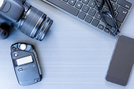top view of a desktop of a photographer consisting on a camera, a keyboard, a photometer, a smart phone and a reading glasses on a grey desk background - suitable for copy spaceの写真素材