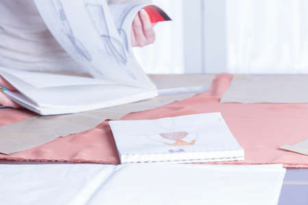 design in a sketchbook on a table with dressmaker leafing through a sketchbook on background at her...