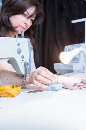 young dressmaker is pinning the fabric seated on a sewing machine at her sewing atelier - focus on...