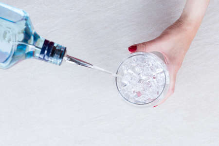 top view of the hands of a woman adding the gin to a gin tonic on a gin tonic preparation session - focus on the ice cubesの写真素材