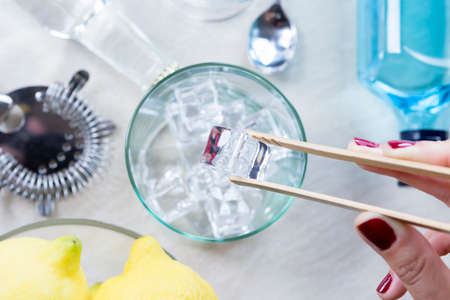 closeup of a woman hand taking ice cubes from an ice bucket with a bamboo ice tongs on a gin tonic session - focus on the ice cubeの写真素材