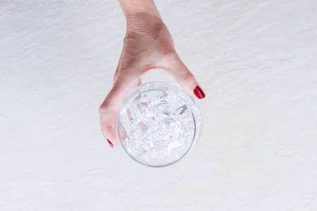 top view of a woman hand holding a balloon glass full of ice cubes on the glass chilling process on a gin tonic preparation session - focus on the ice cubesの写真素材