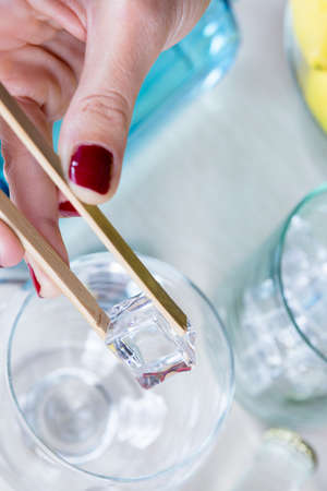 closeup of a woman hand holding an ice cube with a bamboo ice tongs on a gin tonic preparation session - focus on the ice cubeの写真素材