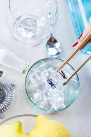 detail of a woman hand taking ice cubes from an ice bucket with a bamboo ice tongs on a gin tonic session - focus on the ice cubeの写真素材
