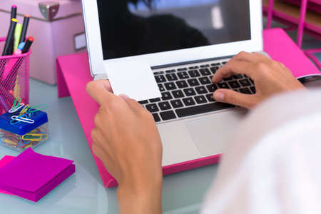 closeup of the hands of a woman holding a visit card while is working with a laptop on a working desk - focus on the left index fingerの写真素材