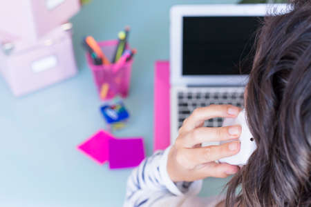 rear view of a woman speaking on a mobile phone while is working on a working desk - focus on the middle fingerの写真素材