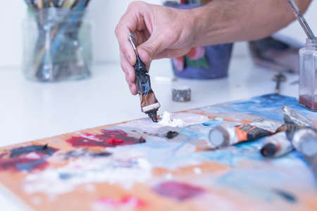 detail of the hand of a male painter adding paint to the palette at his painting studio - focus on paintの写真素材
