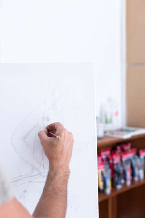 hand of a male painter drawing with a pencil on canvas at his painting studio - focus on the drawingの写真素材