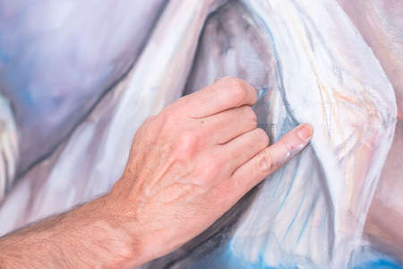 detail of the hand of a painter painting with chalk on canvas - focus on little fingerの写真素材