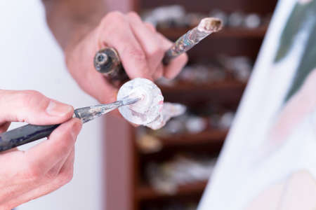 closeup of a hand of a painter taking paint with a paintbrush from a paint tube - focus on the paintbrushの写真素材
