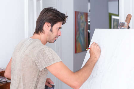 young man drawing with a pencil on canvas at his painting studio - focus on the eyeの写真素材