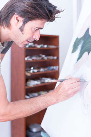 young man painting on canvas at his painting studio - focus on the eyeの写真素材