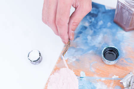 top view of the hand of a male painter mixing paint with the palette knife over the palette at his painting studio - focus on right index fingerの写真素材