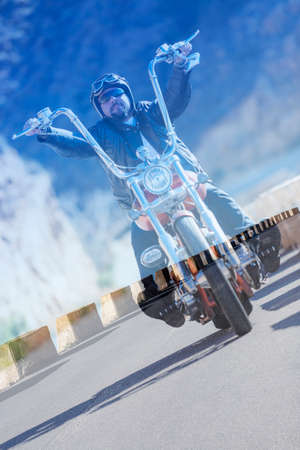 double exposure of a chopper motorcyclist driving his motorcycle by a mountain road on a asphalt highway backgroundの写真素材