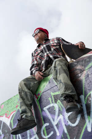 bottom view of an old man skater sitting on a skate park holding his skateboard - focus on the face