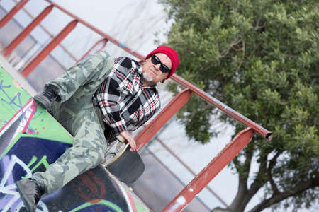 portrait of an old man skater sitting with his skateboard at a skate park - focus on the face