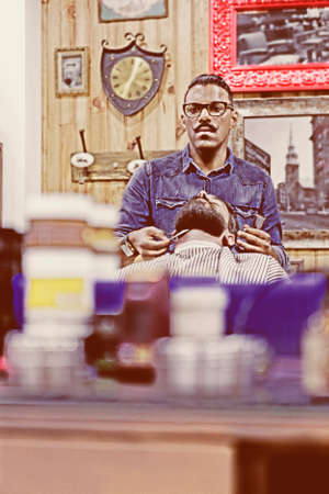 reflection in a mirror of a barber shaving a beard of a customer on a barber shop focus on the barber faceの写真素材