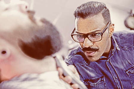 young barber shaving a beard of a customer in a barber shop - focus on the left eyeの写真素材