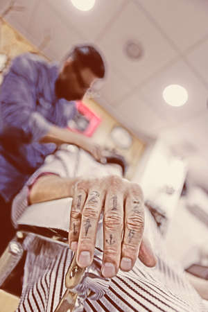 detail of the tattooed hand of a costumer on a beard shaving session sitting on a chair on a barber shop - focus on the handの写真素材