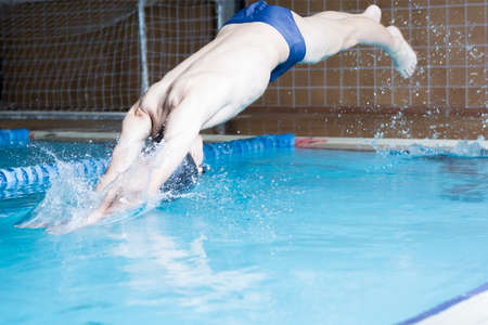 male swimmer is diving head first from the edge of an indoor swimming pool  - focus on the right armの写真素材
