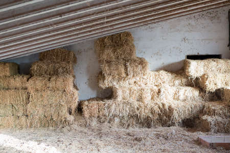 stacked hay bales in the barn of a horse stable - useful as a background - focus on the center of the imageの写真素材