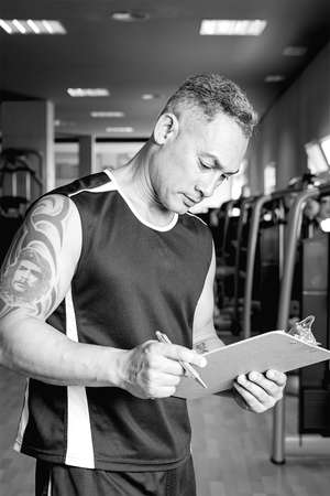 personal trainer holding a clipboard checking the exercise routine at the gym - focus on the right eyeの写真素材
