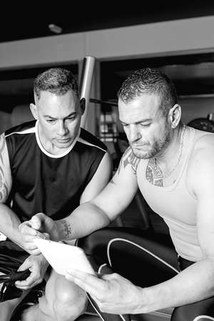personal trainer explaining an exercise routine to young man with a tablet at the gym - focus on the trainer faceの写真素材