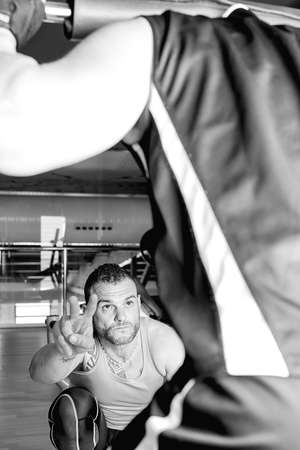 personal trainer helping young man making squat exercise with bar - at the gym - focus on the trainer faceの写真素材