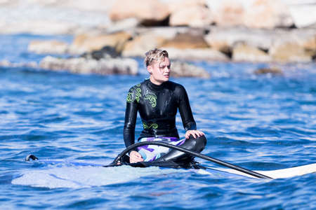 young woman windsurfer is resting upon the windsurf board on a windsurfing session on the sea - focus on the faceの写真素材