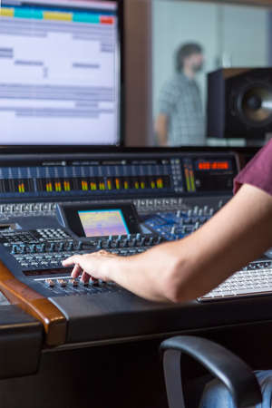 hand of a sound engineer adjusting a sound mixing desk while a singer is rehearsing at the recording studio - focus on the handの写真素材
