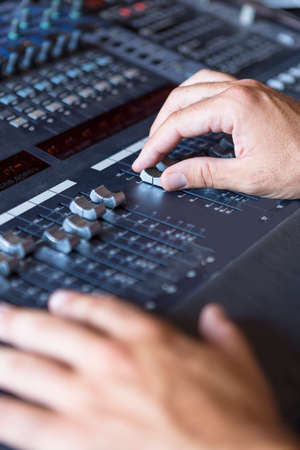 closeup of the hands of a sound professional adjusting a sound mixing desk at the recording studio -...