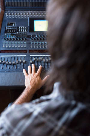subjective view of a hand of a sound engineer adjusting a sound mixing desk at the recording studio - focus on the middle fingerの写真素材