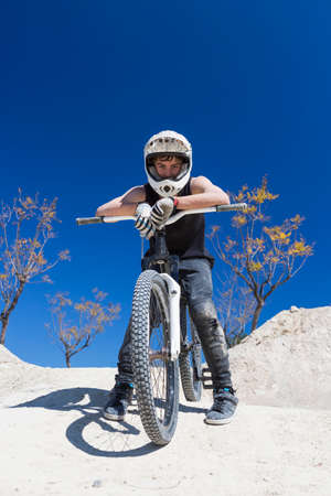 portrait of a young man BMX biker resting sitting on his bike on a BMX session in the mountain - focus on the faceの写真素材