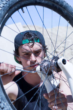 closeup of a young man BMX biker fixing the wheel of his bike on a BMX session in the mountain - focus on the right eyeの写真素材
