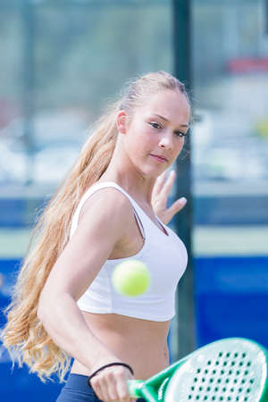 young woman playing a paddle match hits the ball backhand in an outdoor court - focus on the faceの写真素材