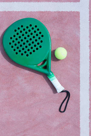 view from above of a green paddle racket and a ball in the line of a clay paddle tennis court useful as a background - focus on the center of the imageの写真素材
