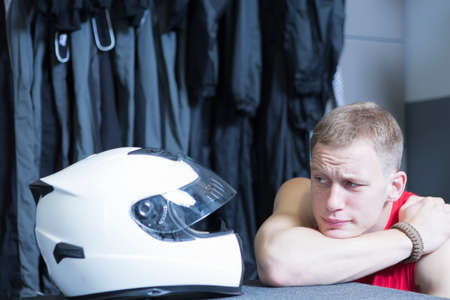 comical image of a young man looking at his helmet before starting a race in an outdoor go karting circuit - focus on the left eyeの写真素材