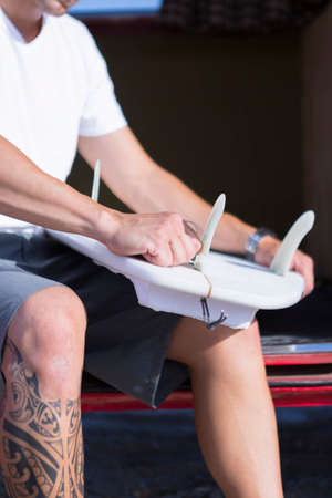 detail of the hands of a young man is preparing a surfboard sitting on a classic van on a surf session on the beach - focus on the right handの写真素材